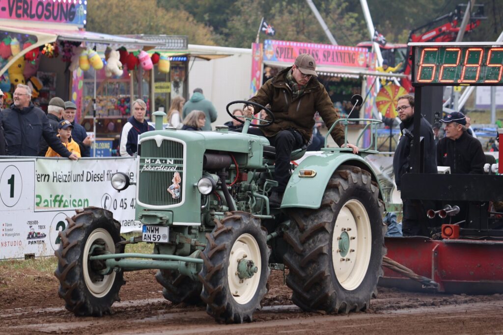 Grüner Oldtimer-Trecker mit angehobenem Vorderrad, Publikum im Hintergrund